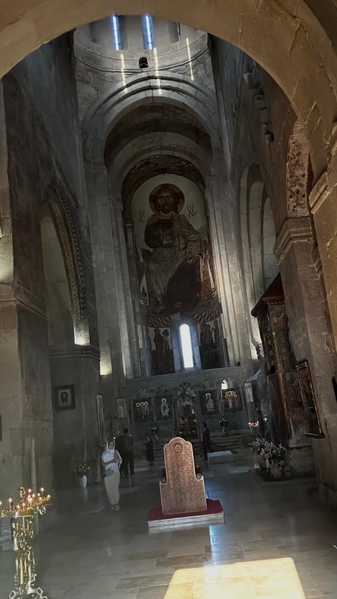 Screenshot - عروبة الاخباري | Oroba News Interior of a stone church with tall arches and a large central mural of Jesus Christ on the apse.