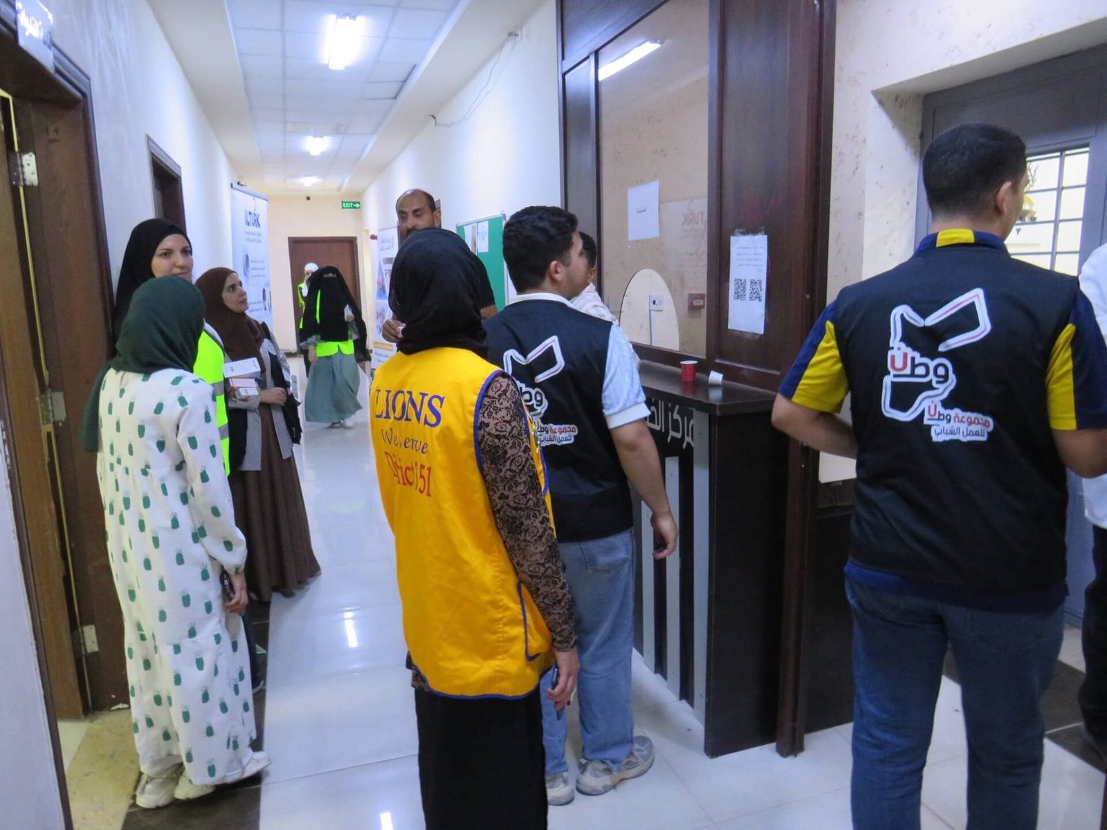 771802317_122373550364016148_8452782026360831880_n - عروبة الاخباري | Oroba News Group of volunteers in a hallway near a registration desk, wearing bright vests with logos.