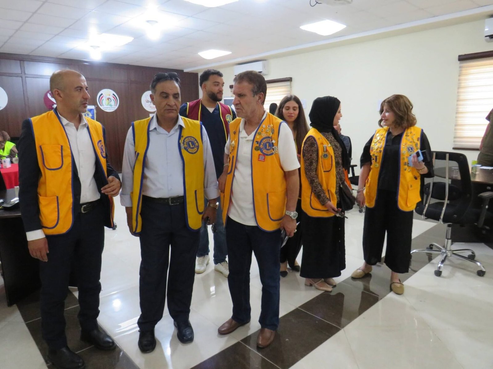 772021187_122373550322016148_6325719074639484251_n - عروبة الاخباري | Oroba News Lions Club members in yellow vests standing indoors, conversing at a meeting event.