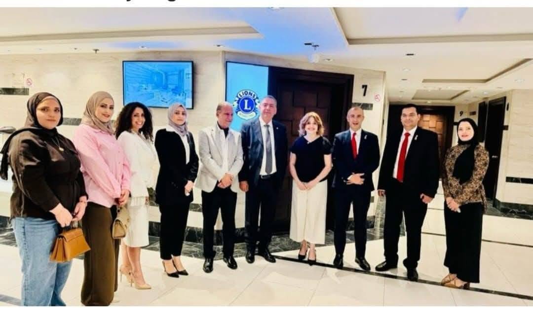 774897965_122374744136016148_3334152079001889363_n - عروبة الاخباري | Oroba News Group of men and women in business attire standing in a lobby with a Lions Club logo in the background, posing for a photo.