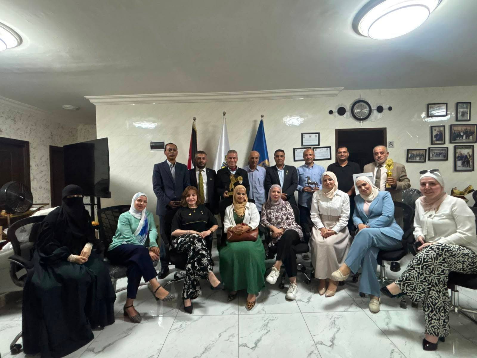 775013650_122374745114016148_7884762527316678042_n - عروبة الاخباري | Oroba News Group of men and women in an office posing for a photo, several holding trophies; flags and framed certificates on the wall behind them.