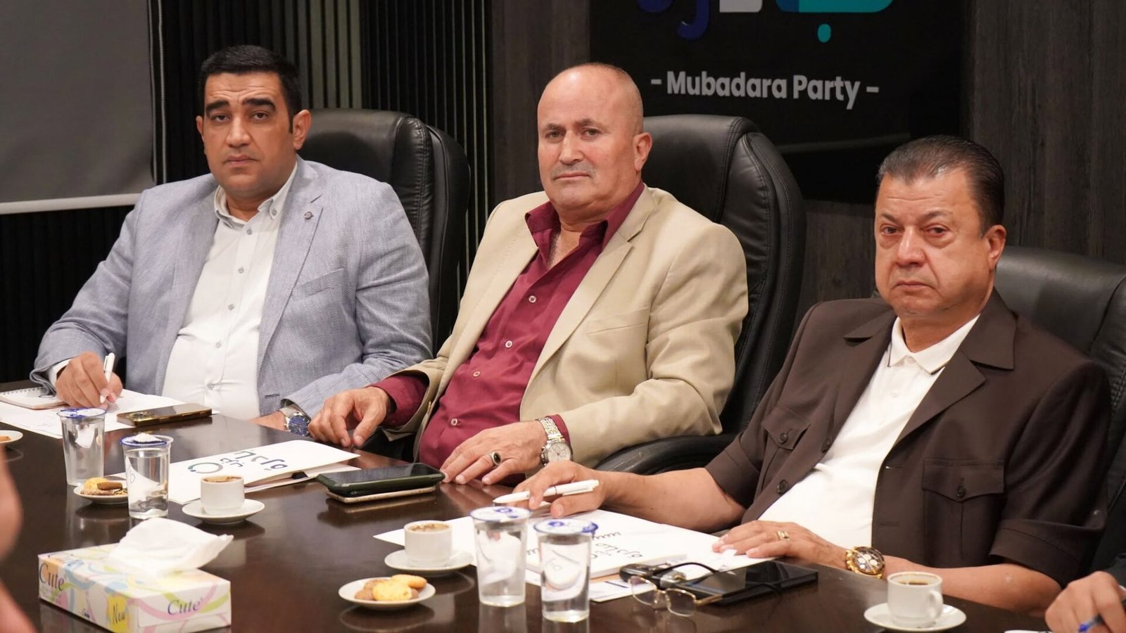 775260356_122145932691082282_5102492655619353553_n - عروبة الاخباري | Oroba News Three men in business attire sit at a conference table with papers, pens, and coffee during a meeting.