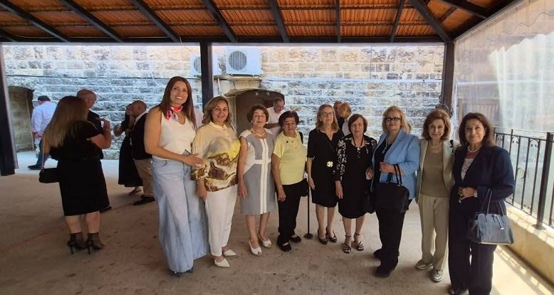 Group of women posing for a photo on a covered patio during a social gathering, smiling at the camera in smart casual attire.