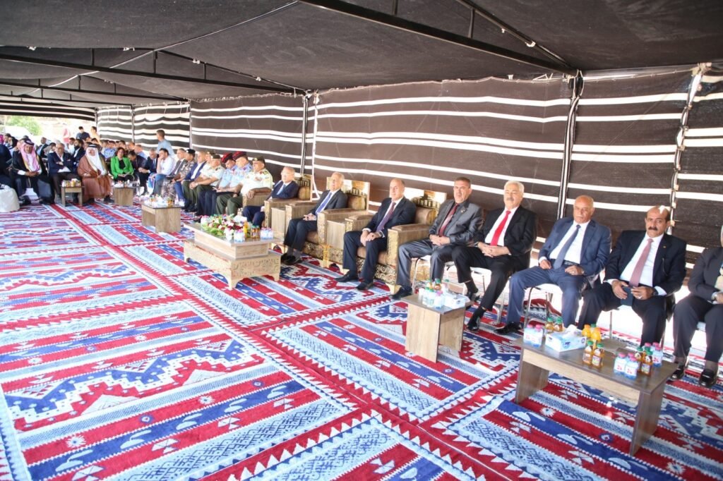 FYz59aSx7M25ZokcsCUwhNSh6TQDNjMmLuHimprG - عروبة الاخباري | Oroba News A row of men in suits and uniforms seated inside a black-striped tent during a formal meeting, with coffee and water bottles on small tables in front and colorful patterned floor mats beneath them.
