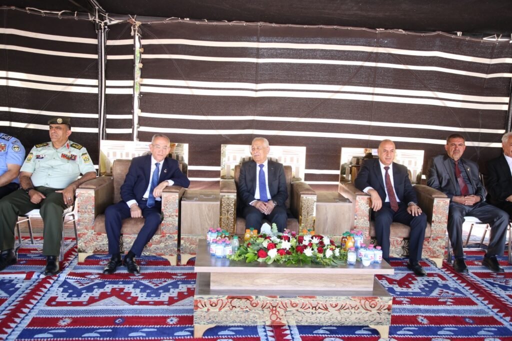 NASaRAwzcmD8rjxnFng8cfqathfWsrzbPczAMuHF - عروبة الاخباري | Oroba News Group of dignitaries and military officers seated in a row under a striped tent, with a flowered centerpiece and beverages on a low table in front.