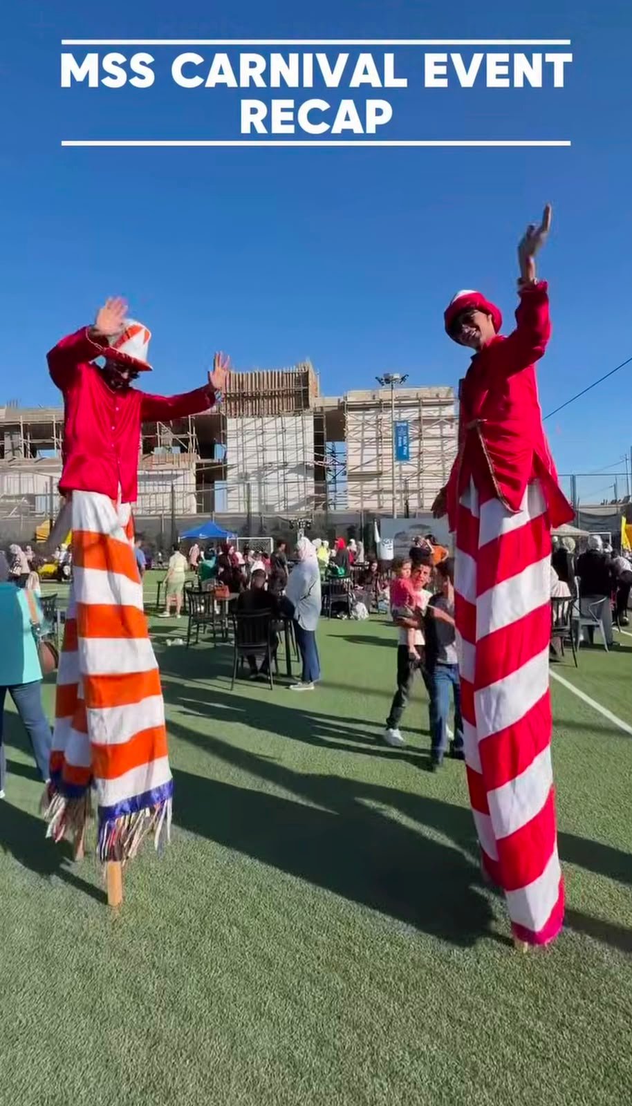 WhatsApp Image 2026-08-01 at 33334 PM 3 Two performers on stilts in red outfits with bold striped legs entertain a crowd at an outdoor carnival; a banner above reads 'MSS CARNIVAL EVENT RECAP' as spectators sit and stand on a grassy field with a construction site in the background.