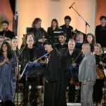 WhatsApp Image 2026-08-04 at 41236 PM 6 - عروبة الاخباري | Oroba News Female singer in a blue gown stands at a microphone at center stage, with a full orchestra and stage lighting behind her.