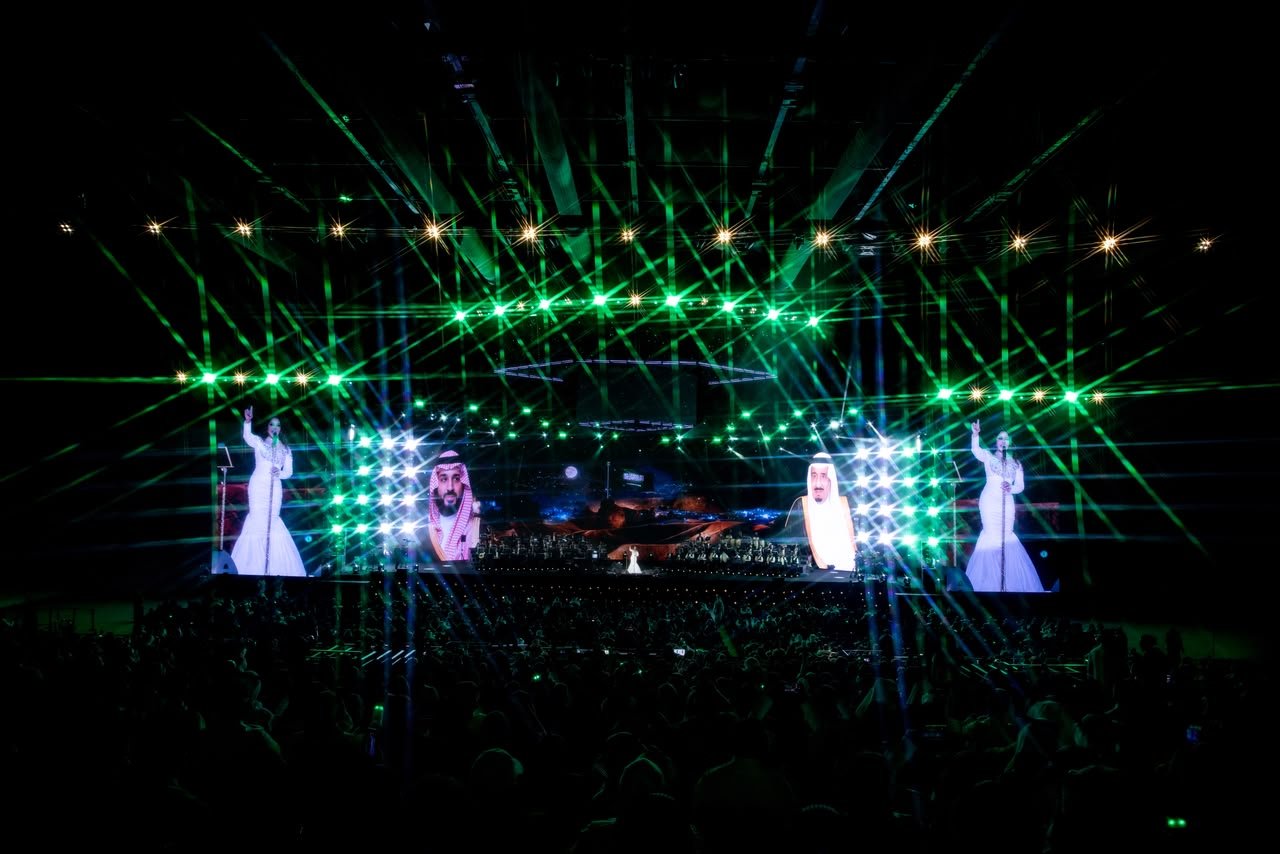 WhatsApp Image 2026-08-04 at 80705 PM2 Concert stage with green laser lights and large screens showing performers and guests, a crowded audience in front.