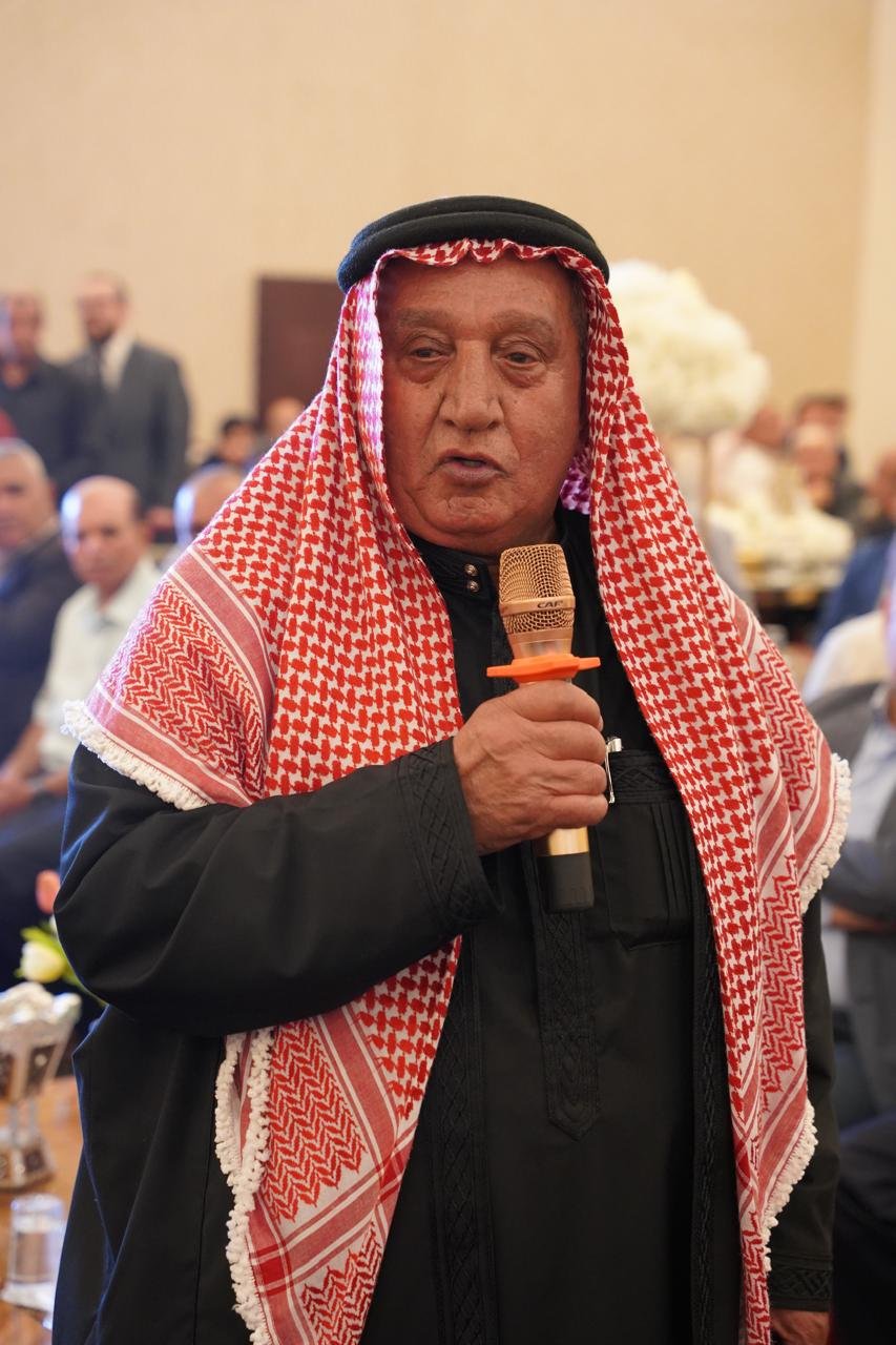 WhatsApp Image 2026-08-05 at 32452 PM1 - عروبة الاخباري | Oroba News Older man wearing a red and white keffiyeh and black thobe speaks into a microphone at a formal event.