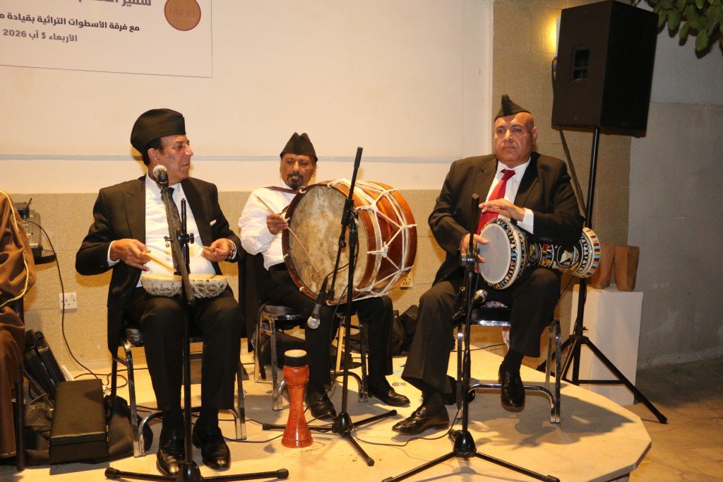 WhatsApp Image 2026-08-06 at 41356 PM - عروبة الاخباري | Oroba News Three men in suits and fez hats perform traditional Arabic drumming on a small stage, with microphones and a banner in Arabic in the background.