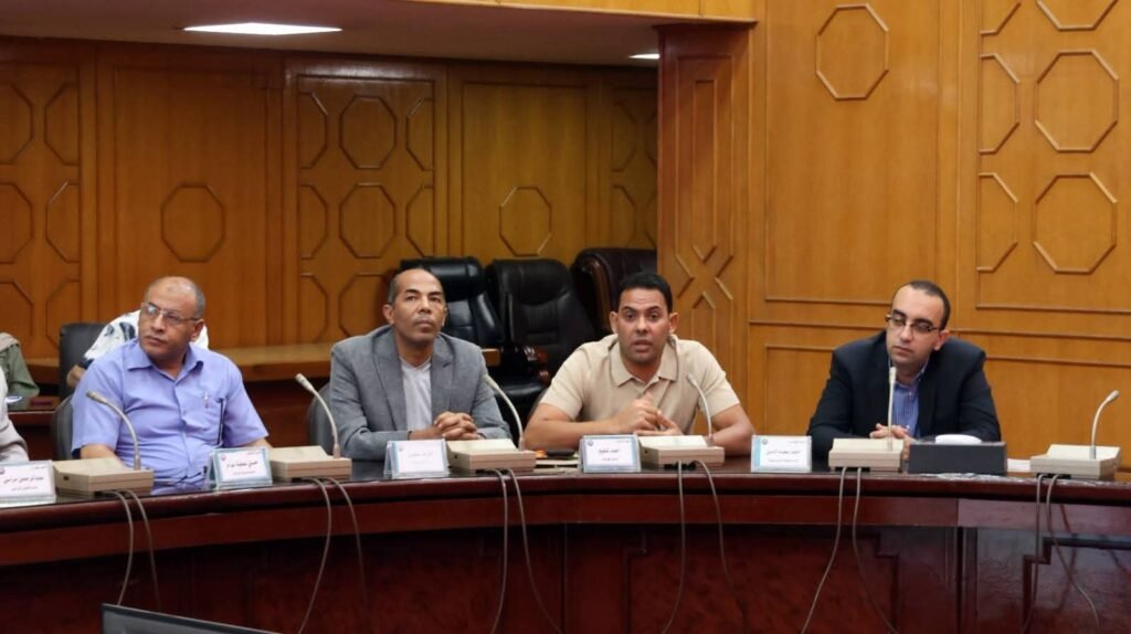WhatsApp Image 2026-08-06 at 63455 PM - عروبة الاخباري | Oroba News Four men sit at a curved wooden conference table with microphones, engaging in a formal panel discussion in a wood-paneled room.