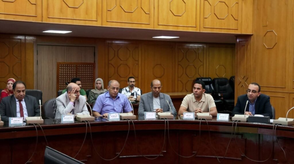 WhatsApp Image 2026-08-06 at 63455 PM1 - عروبة الاخباري | Oroba News Six men seated along a curved wooden conference table in a formal meeting, with nameplates and microphones in front of them.