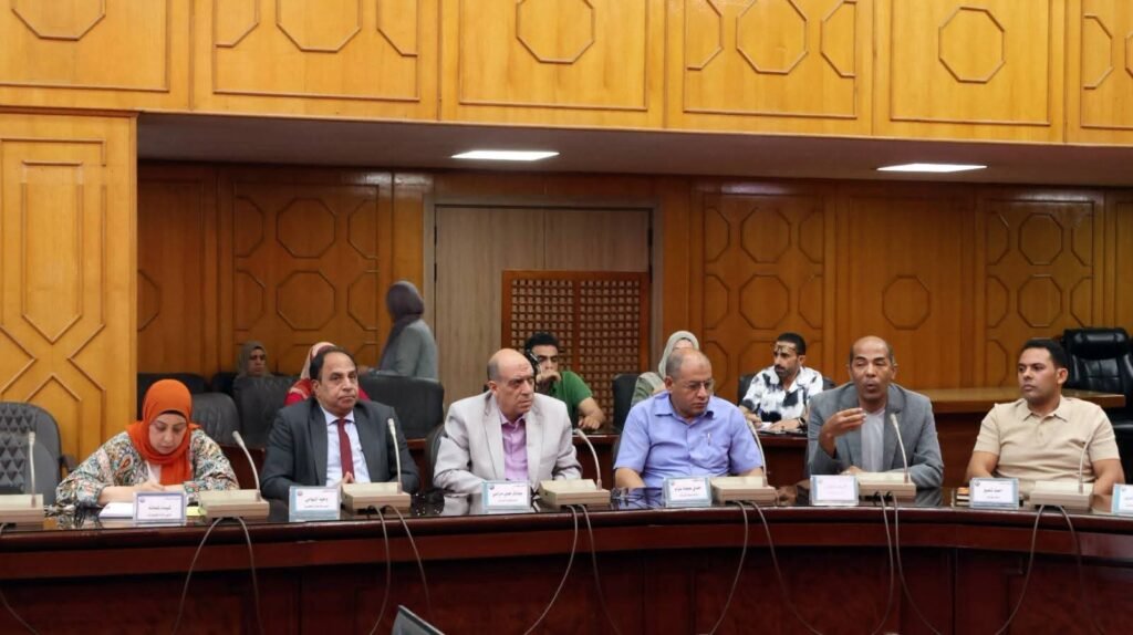 WhatsApp Image 2026-08-06 at 63455 PM2 - عروبة الاخباري | Oroba News Seven panelists seated at a long wooden conference table in a wood-paneled room, some speaking into microphones with nameplates in front.