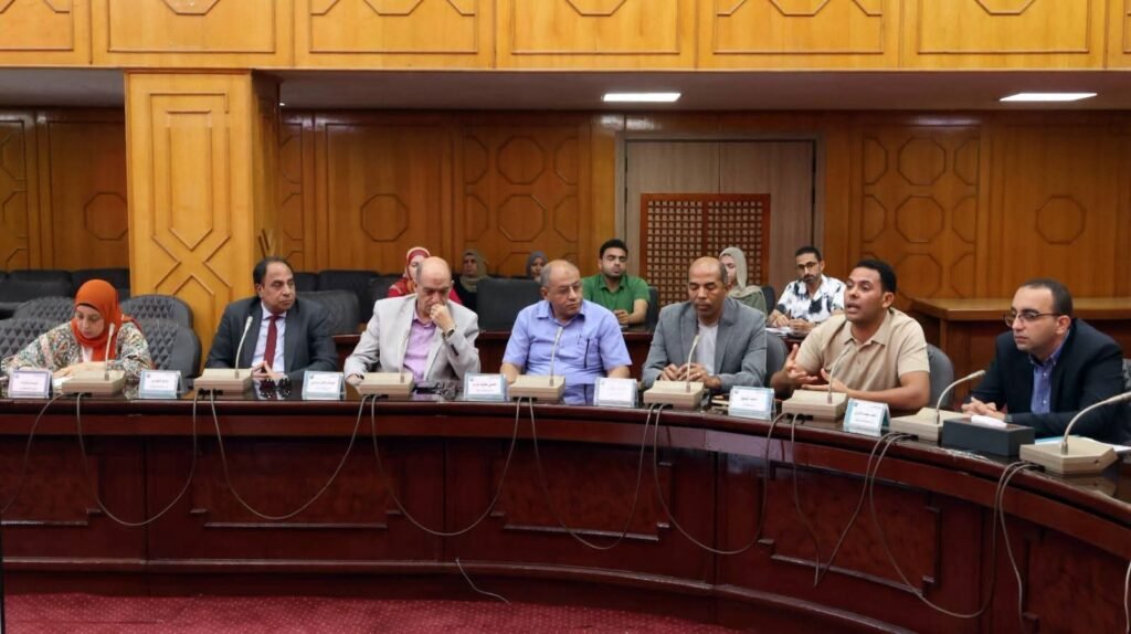 WhatsApp Image 2026-08-06 at 63455 PM3 - عروبة الاخباري | Oroba News Group of professionals seated around a curved wooden conference table in a formal meeting room, microphones and nameplates in front of them,