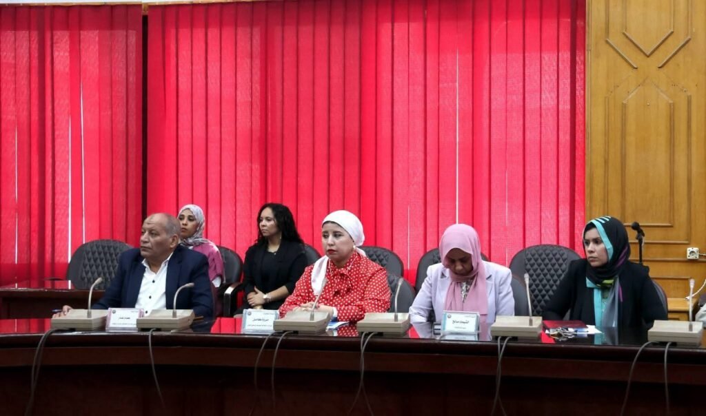 WhatsApp Image 2026-08-06 at 63456 PM - عروبة الاخباري | Oroba News Five people seated at a conference table with microphones and nameplates during a formal meeting, red curtains behind them.