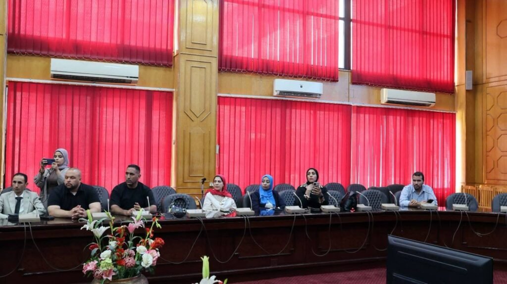 WhatsApp Image 2026-08-06 at 63456 PM1 - عروبة الاخباري | Oroba News Group of people seated along a long conference table in a room with tall red blinds and a flower centerpiece at the front.