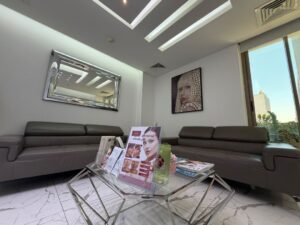 Modern waiting room with gray leather sofas, a glass coffee table displaying magazines, and a wall mirror reflecting ceiling lights.