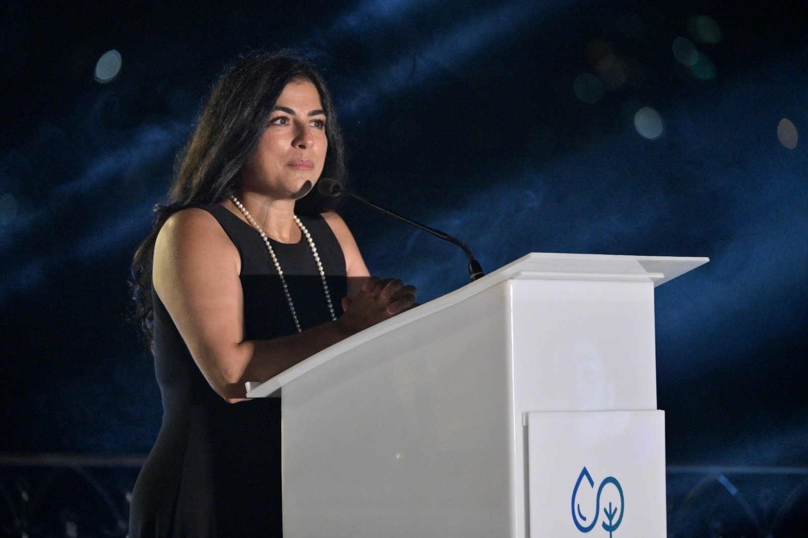 WhatsApp Image 2026-08-07 at 14939 PM 1 - عروبة الاخباري | Oroba News Woman in a black dress with a pearl necklace delivers a speech from a white podium on a dark stage.
