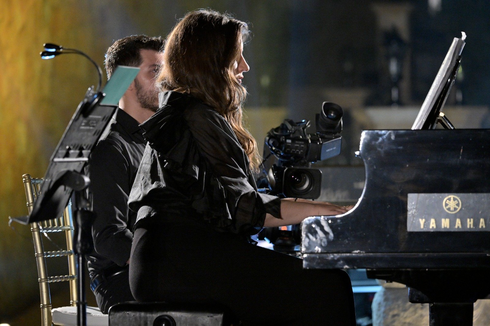 WhatsApp Image 2026-08-07 at 14945 PM 4 - عروبة الاخباري | Oroba News Female pianist in black performs on a Yamaha grand piano while a cameraman films from the side.