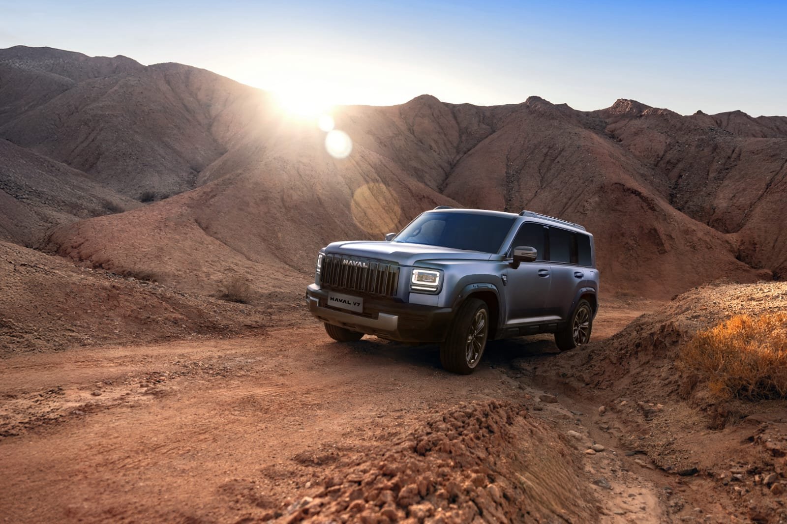 Blue off-road SUV navigating rugged desert canyon as the sun rises behind the hills.