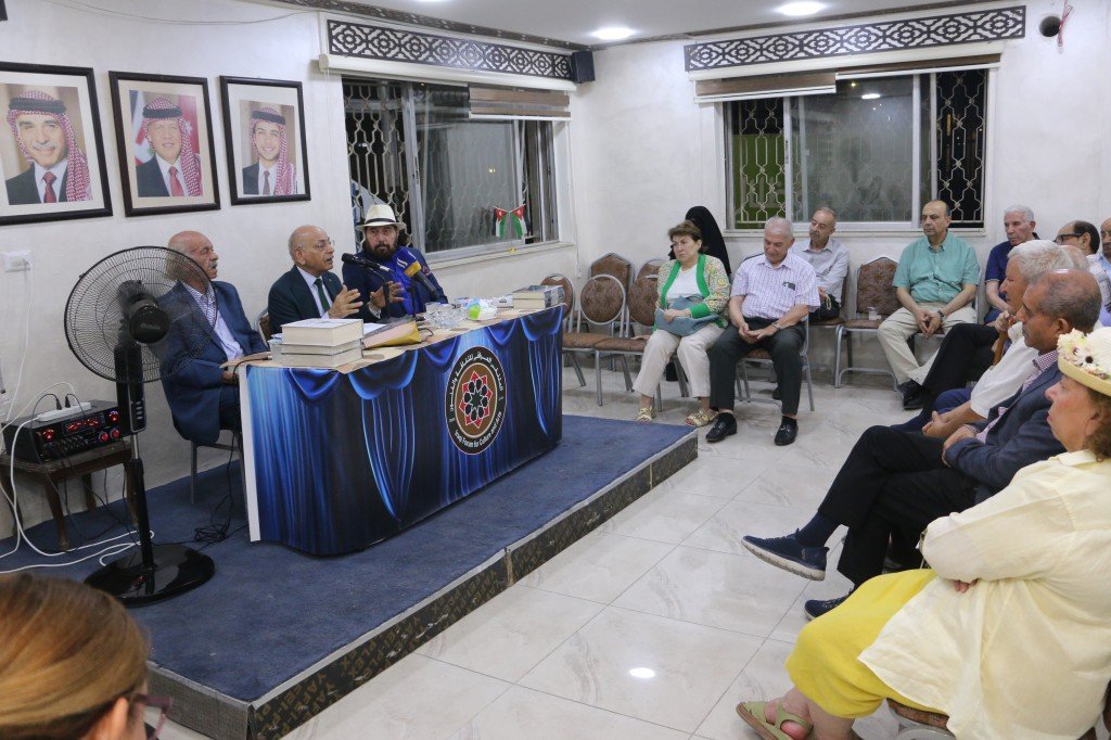 WhatsApp Image 2026-08-10 at 10923 PM - عروبة الاخباري | Oroba News Panel discussion in a small hall with three men seated at a blue-draped table; audience sits in chairs along the wall behind them.