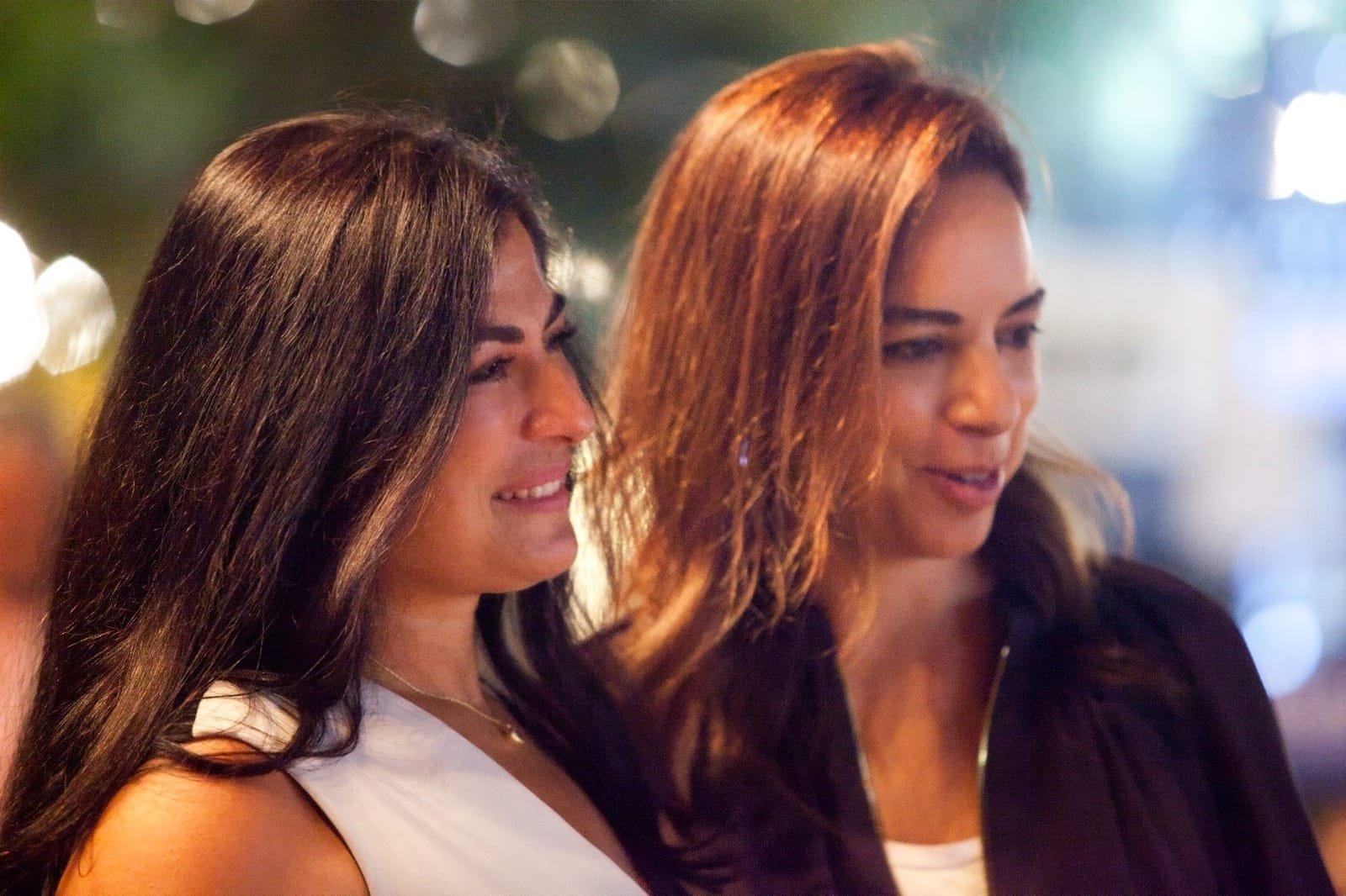 WhatsApp Image 2026-08-10 at 45552 PM - عروبة الاخباري | Oroba News Two women standing close together, smiling softly, in a nighttime urban setting with blurred lights in the background.