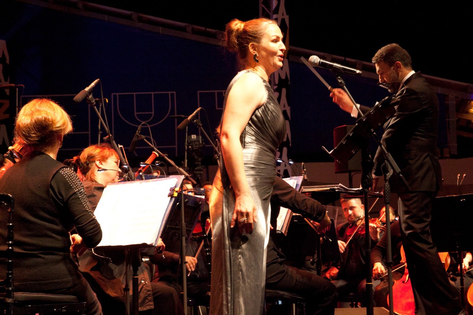 WhatsApp Image 2026-08-10 at 45554 PM 5 - عروبة الاخباري | Oroba News Female singer in a silver gown performs at microphone on stage with an accompanying orchestra behind her.