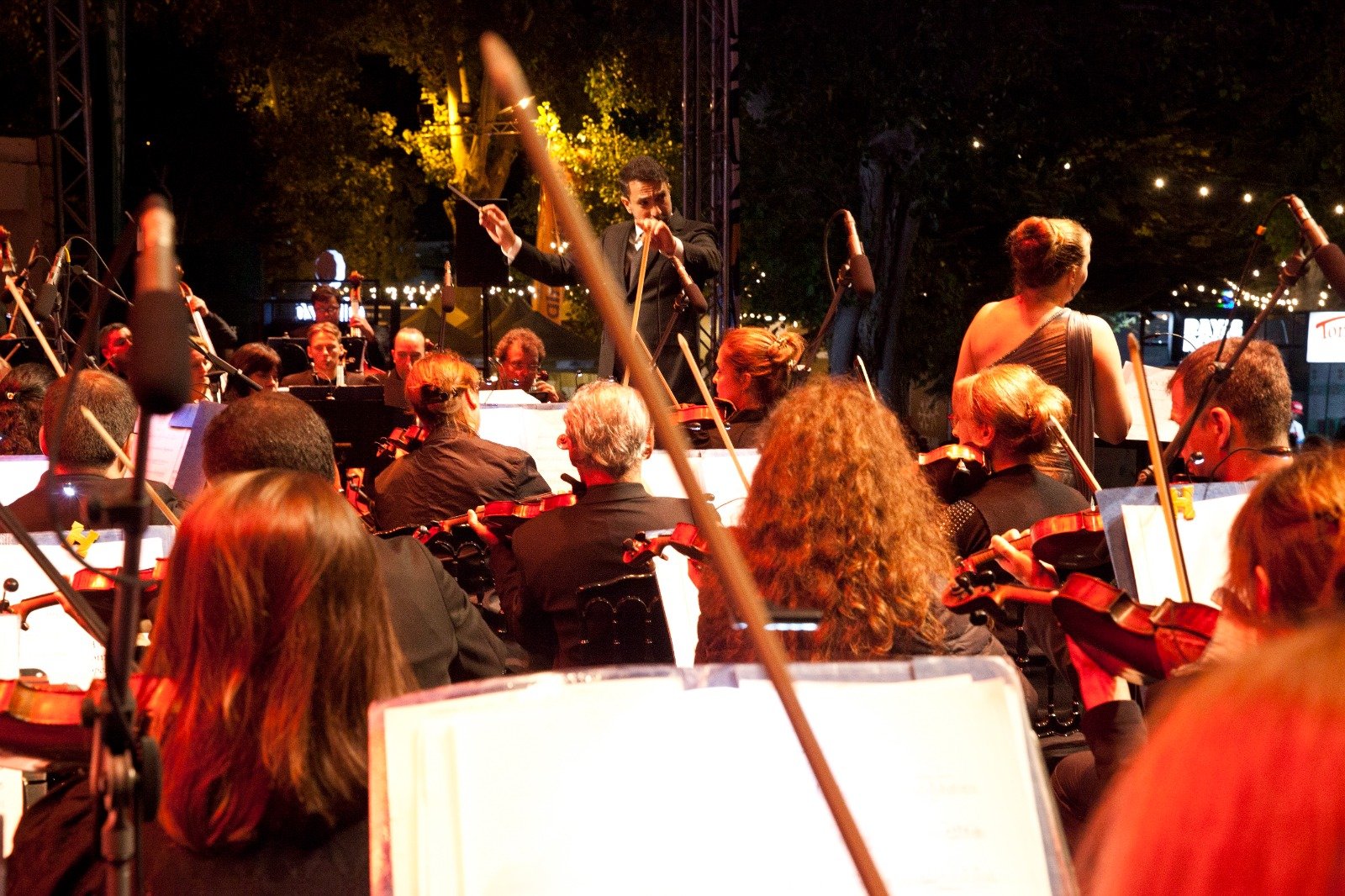 WhatsApp Image 2026-08-10 at 45555 PM 2 - عروبة الاخباري | Oroba News Conductor leading a nighttime outdoor orchestra with string players in the foreground and warm stage lights in the background.