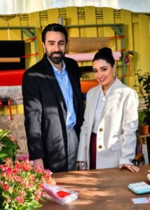 WhatsApp Image 2026-08-11 at 115038 AM1 - عروبة الاخباري | Oroba News Two professionally dressed people smile at the camera in a bright workshop with fabric rolls and plants in the background.