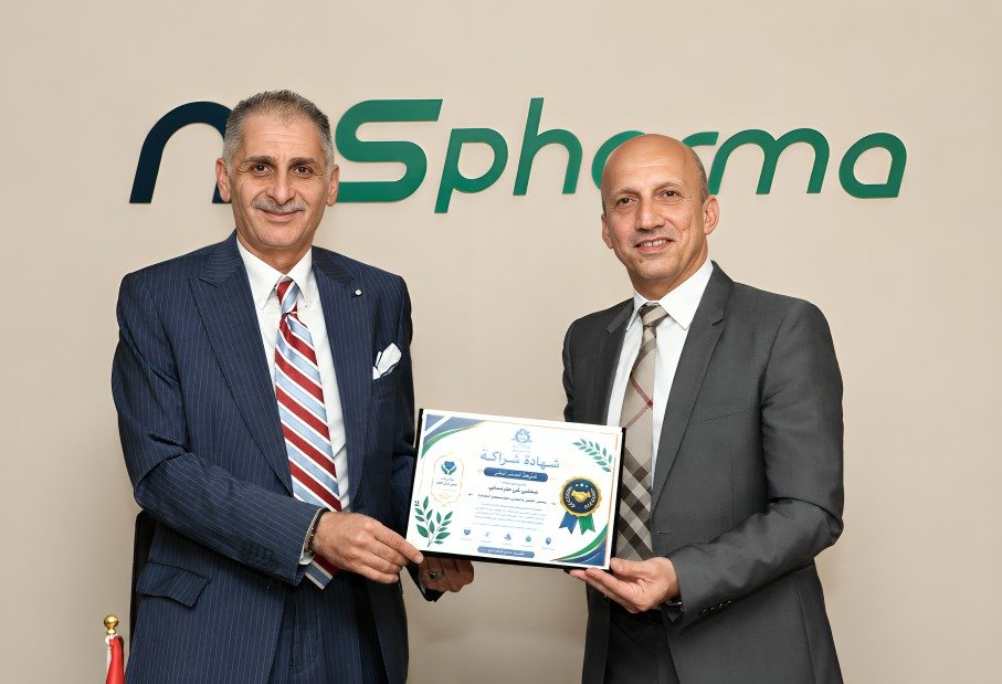WhatsApp Image 2026-08-11 at 44907 PM1 - عروبة الاخباري | Oroba News Two men in suits present a certificate at a formal award ceremony, with a pharma company logo in the background.