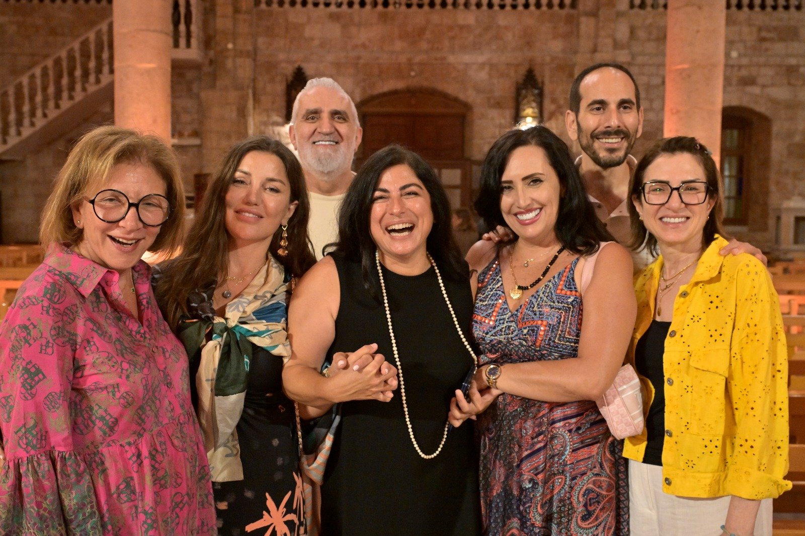 Group of six adults posing together and smiling in a warmly lit stone venue.