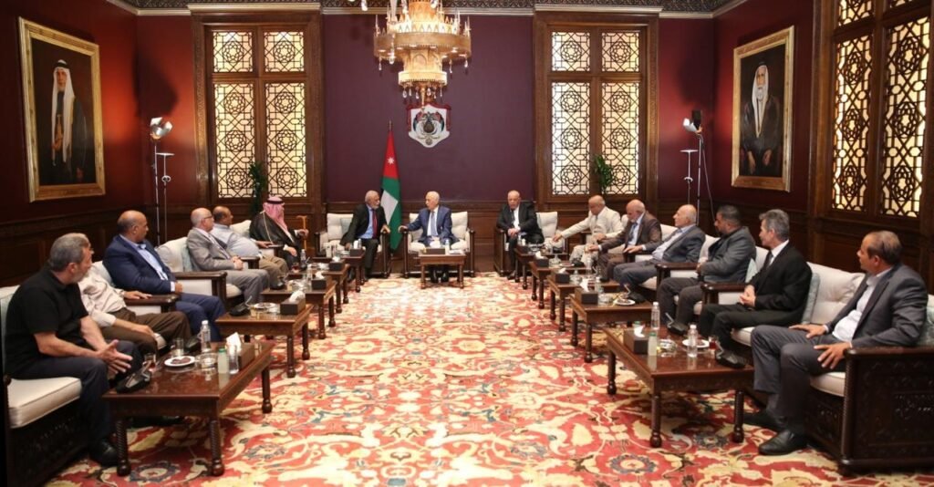 WhatsApp Image 2026-08-19 at 25219 PM1 - عروبة الاخباري | Oroba News Diplomatic meeting in a grand room with two groups of men seated on sofas around low tables, Jordan flag visible in the center and a chandelier overhead.