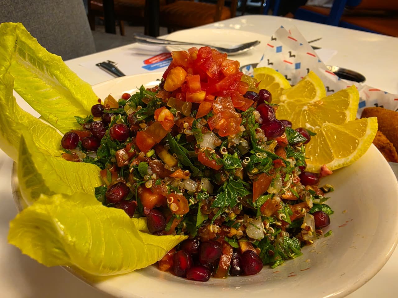 Quinoa salad with tomatoes, cucumbers, herbs, and pomegranate, plated with lettuce and lemon wedges.