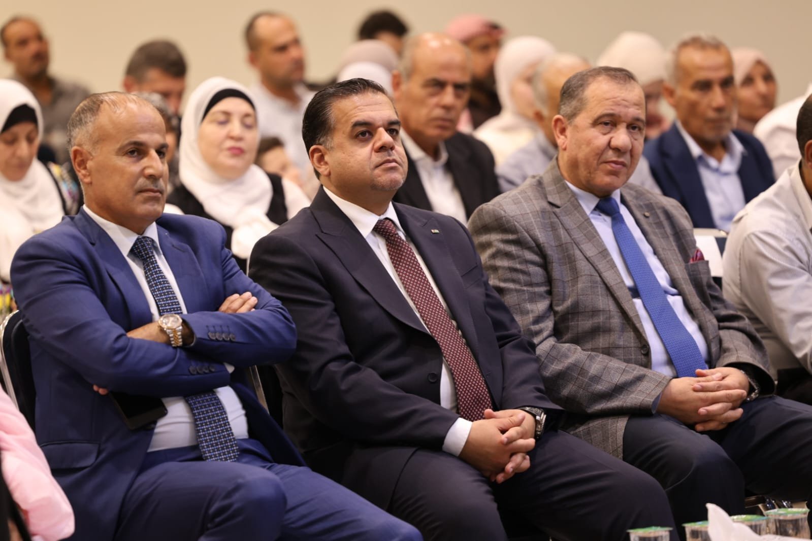 WhatsApp Image 2026-08-23 at 110030 PM - عروبة الاخباري | Oroba News Three men in formal suits seated in an audience at a conference, listening attentively.