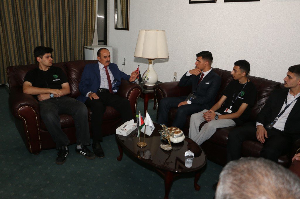 WhatsApp Image 2026-08-23 at 120306 AM - عروبة الاخباري | Oroba News A group of men sits on leather sofas in a living room, one in a blue suit speaking while others listen attentively around a coffee table with flags and a lamp nearby.