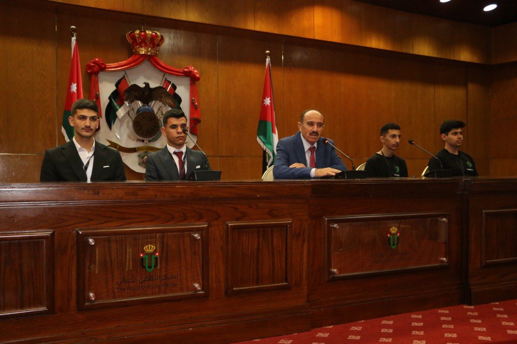 WhatsApp Image 2026-08-23 at 120309 AM - عروبة الاخباري | Oroba News Panel of five at a wooden dais in a formal meeting room, with Jordanian flags and an official crest behind them; a man in a blue suit speaks into a microphone.