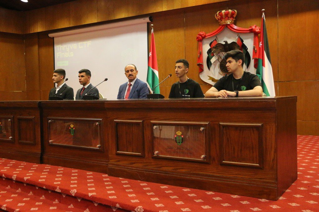 WhatsApp Image 2026-08-23 at 120310 AM - عروبة الاخباري | Oroba News Five men sit behind a long wooden panel on a stage, microphones in front, with a Jordan flag and crest backdrop behind them.