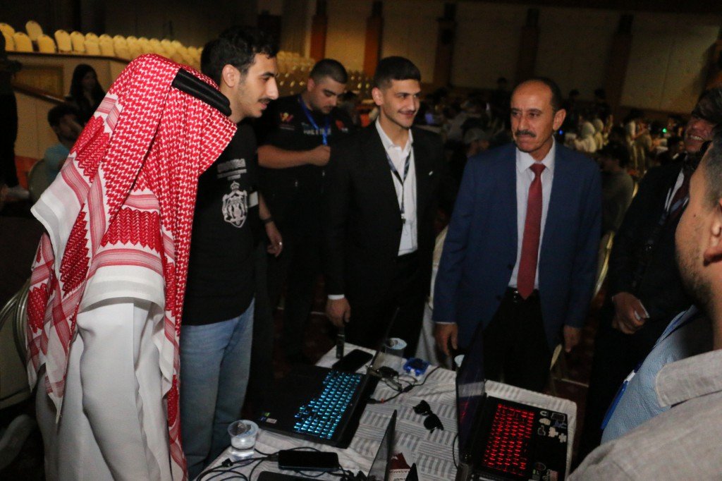 WhatsApp Image 2026-08-23 at 120314 AM1 - عروبة الاخباري | Oroba News Group of men gathered around a tech table with laptops at an event; one wears a red-and-white keffiyeh.