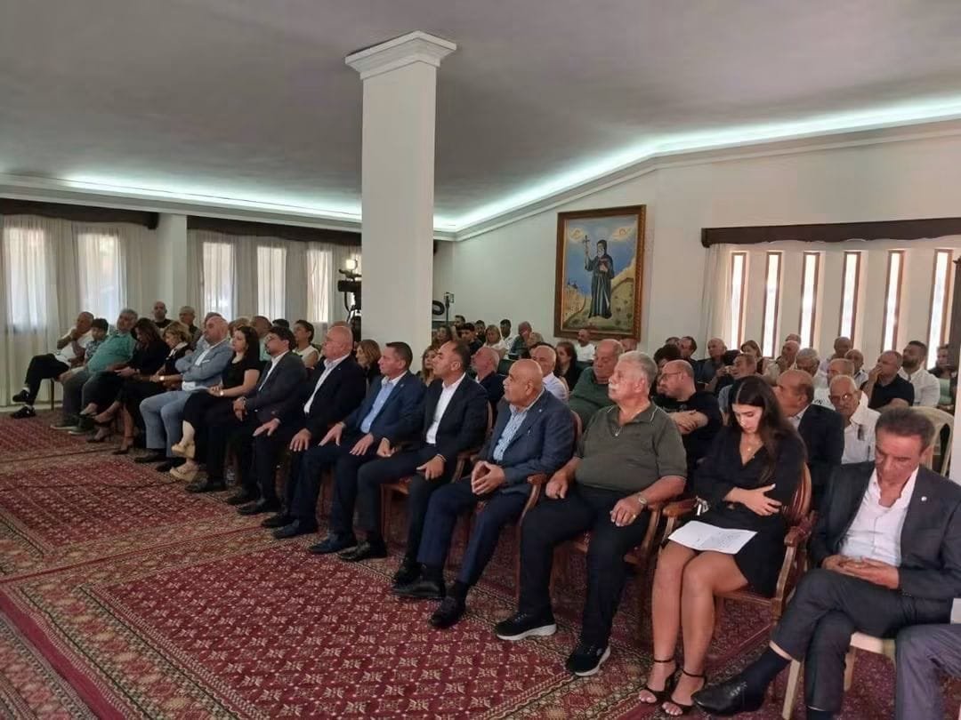 Group of professionally dressed people seated in rows at a formal event in a conference room.