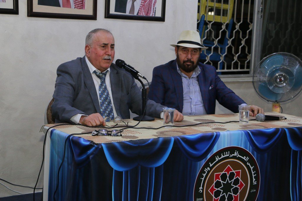 WhatsApp Image 2026-08-25 at 94609 PM - عروبة الاخباري | Oroba News Two men in suits sit at a panel table with microphones during a discussion; a banner with a circular emblem hangs in front.
