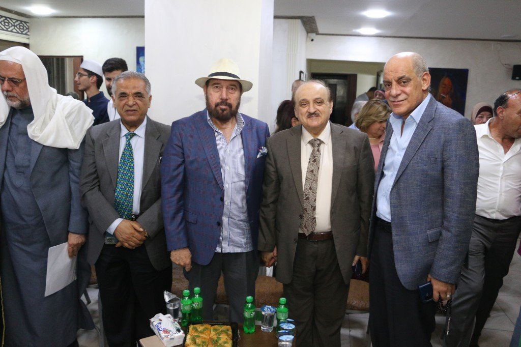 WhatsApp Image 2026-08-25 at 94612 PM - عروبة الاخباري | Oroba News Group of men in suits posing for a photo at an indoor event, with snacks and bottles on a table in front of them.