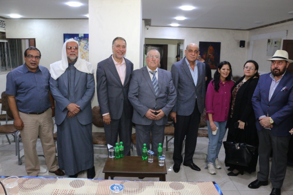 WhatsApp Image 2026-08-25 at 94614 PM - عروبة الاخباري | Oroba News Nine adults stand together for a formal group photo in a bright room, around a table with bottled drinks in front of them.