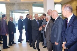 Group of men in suits lined up in a lobby, handshake greeting at a formal event.