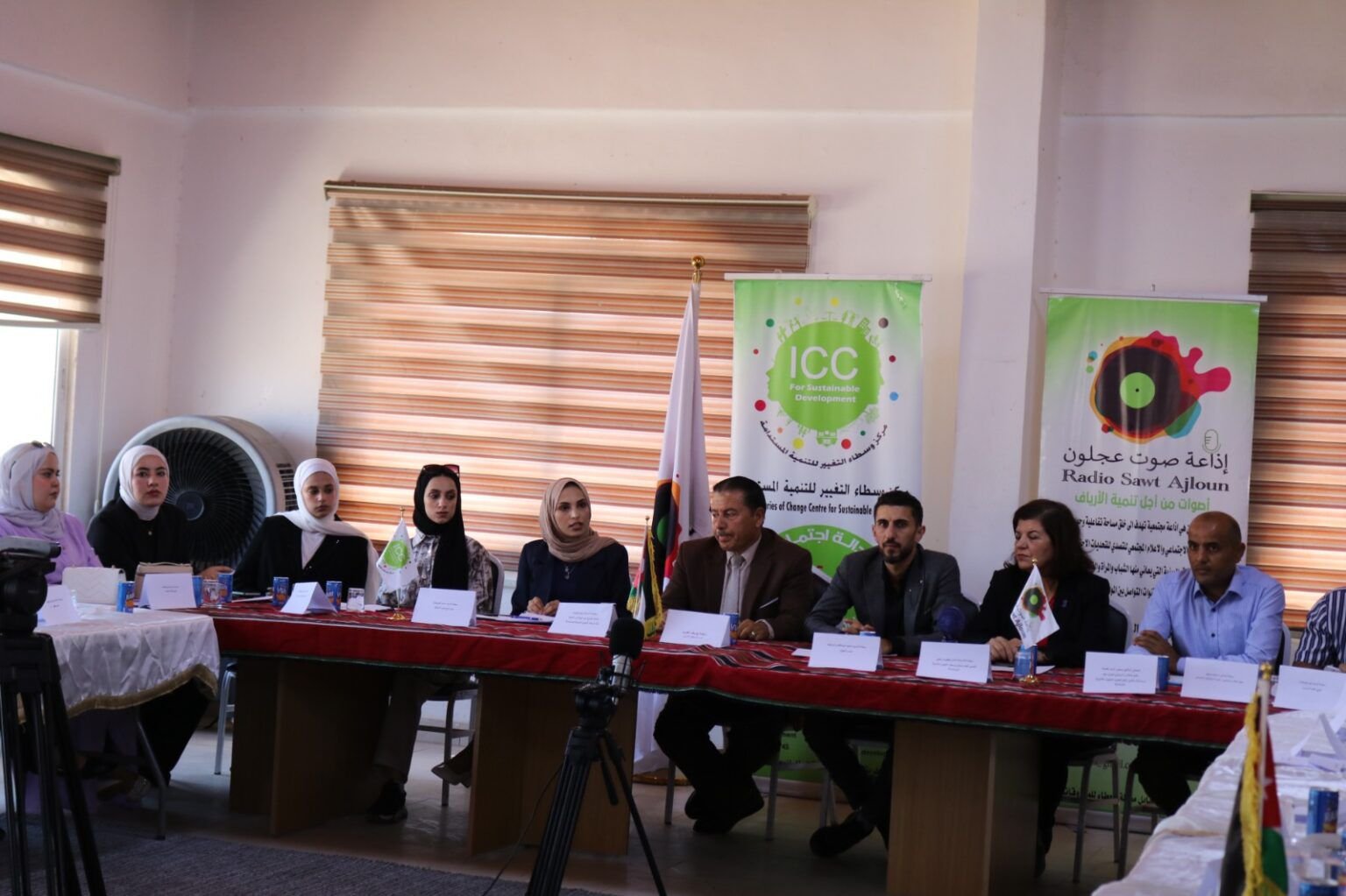 Panel of men and women seated at a long conference table with banners reading ICC in the background and flags nearby.