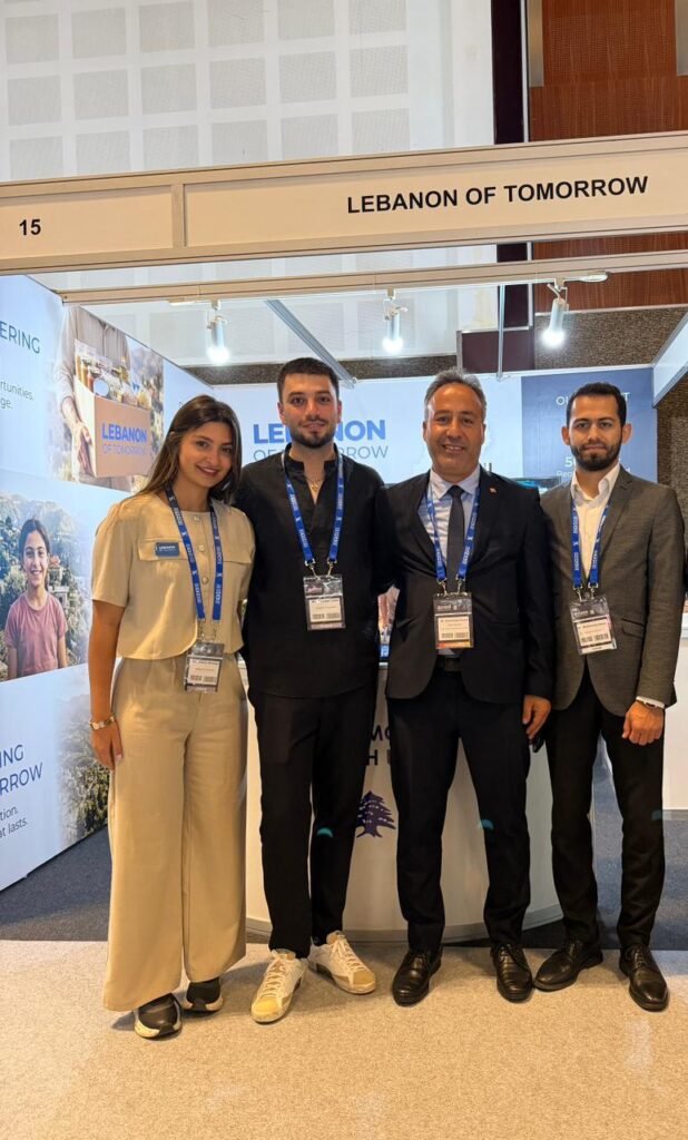 Four people stand together at a trade show booth labeled 'LEBANON OF TOMORROW', wearing lanyards and name badges.
