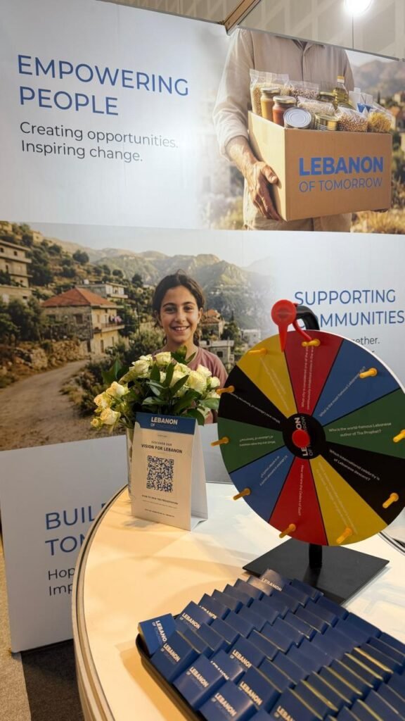 Young girl holding flowers at a Lebanon charity booth with a colorful prize wheel and brochures on the table.