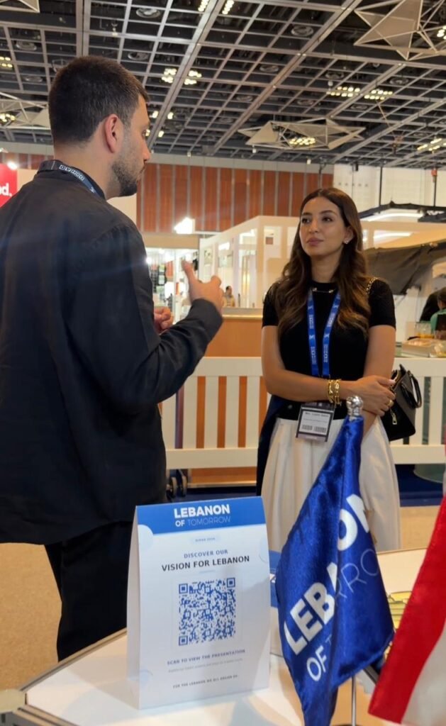 Man and woman talking at a Lebanon of Tomorrow booth, with a QR code sign on the table in front of them.