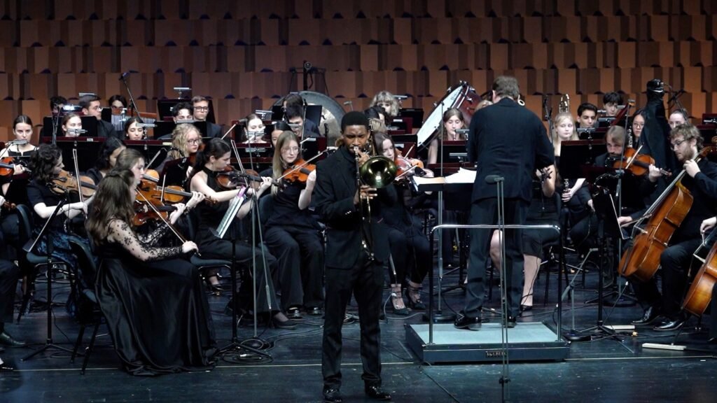 WhatsApp Image 2026-08-29 at 123201 PM 2 - عروبة الاخباري | Oroba News Conductor leads a full orchestra on stage, with violinists and other musicians in black formal attire performing behind him.