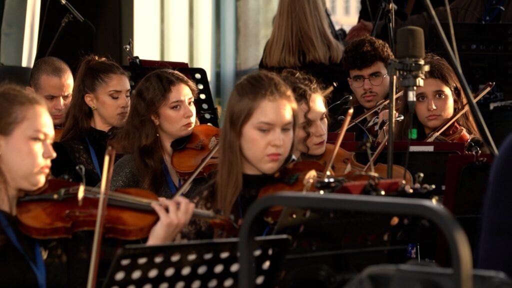WhatsApp Image 2026-08-29 at 123201 PM 5 - عروبة الاخباري | Oroba News Group of young violinists in an orchestra, focused on their sheet music during a performance.