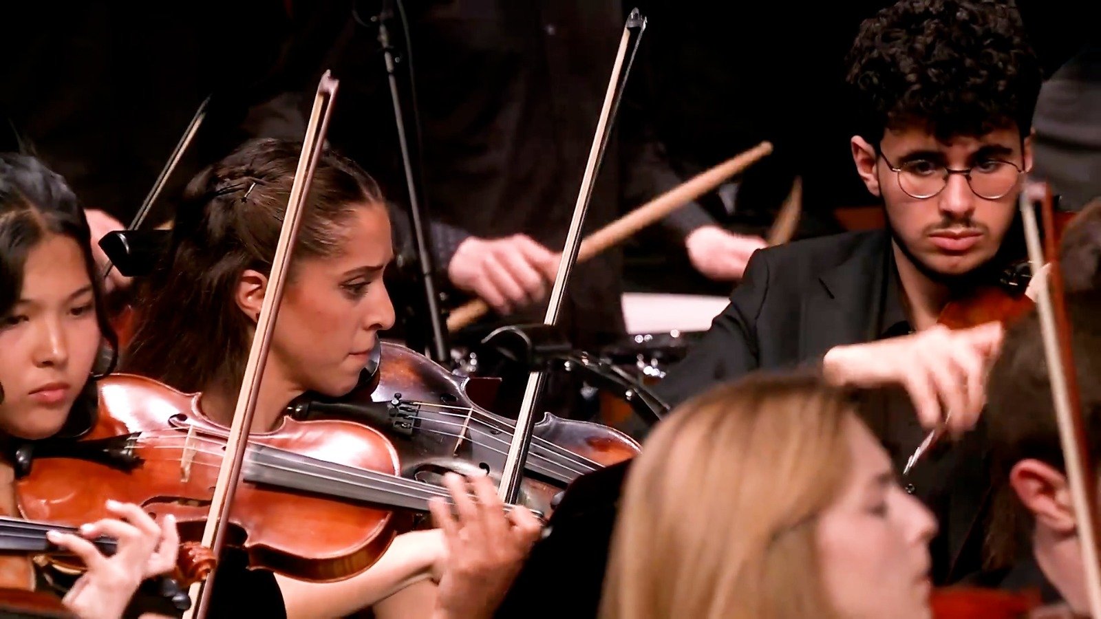 WhatsApp Image 2026-08-29 at 123203 PM 1 - عروبة الاخباري | Oroba News A section of an orchestra playing violins on stage, with focused musicians.